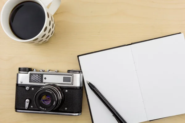 Old camera, notebook, pen and a cup of coffee on wooden surface