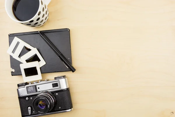 Old camera, notebook, pen and transparency slides on wooden surface