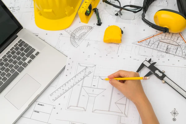 Hand over Construction plans with yellow helmet and drawing tool