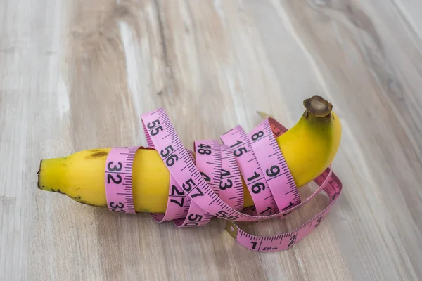 Measure tape wrapped around  banana on wood table .