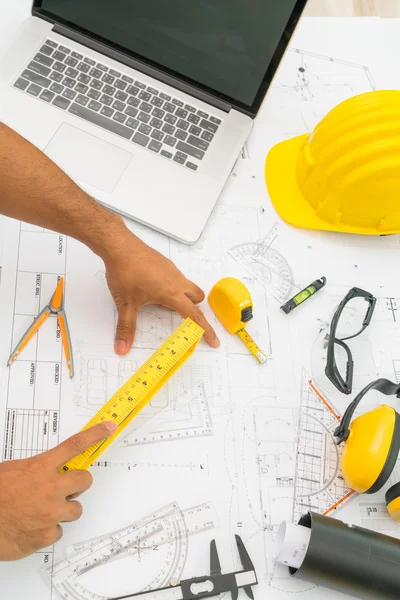 Hand over Construction plans with yellow helmet and drawing tool