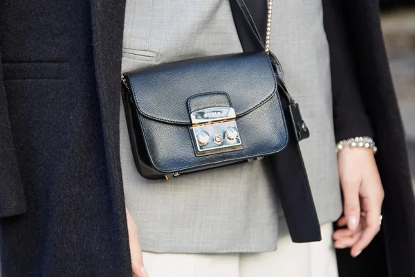 Woman poses for photographers with Furla black leather bag, street style