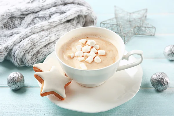 Cup of hot cacao with marshmallow, cookies and warm scarf on blue table