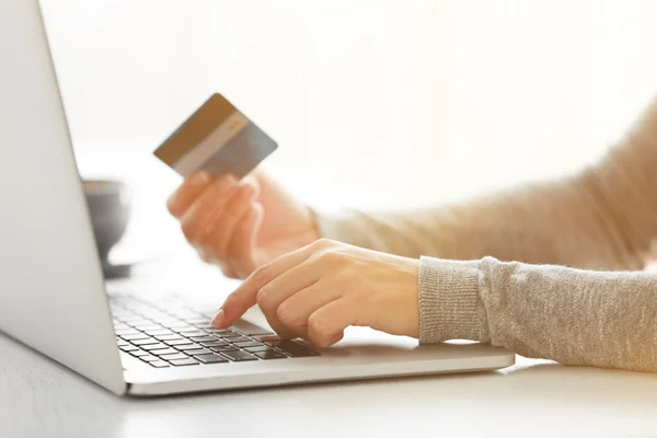 E-commerce concept. Woman with credit card, laptop and cup of coffee, close up