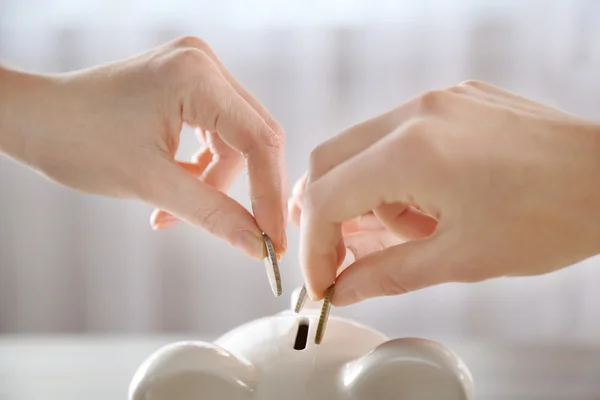 Hands putting coins into piggy bank