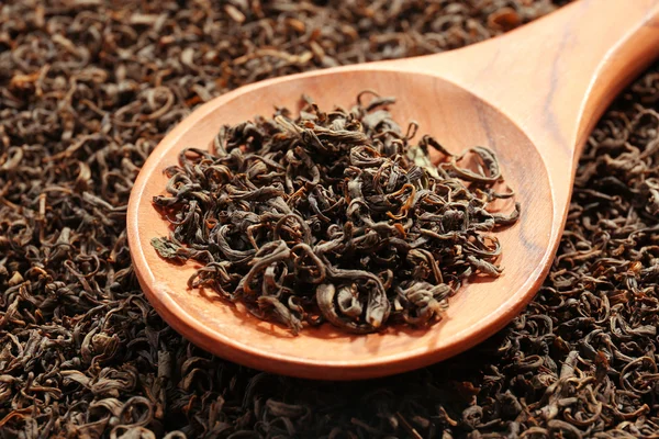 Pile of dry tea with wooden spoon, close up