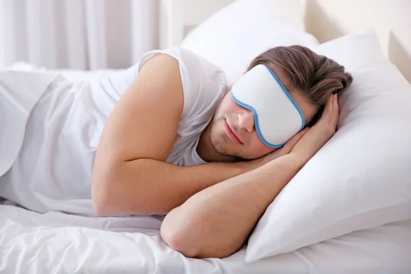 Young man sleeping with blindfold in bed at home