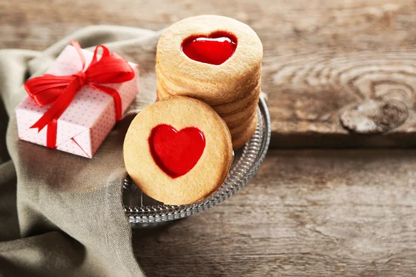 Assortment of love cookies with gift and cloth on wooden background, closeup