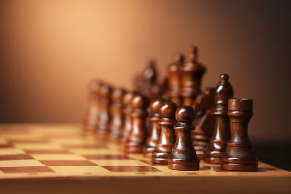 Chess pieces and game board on brown background