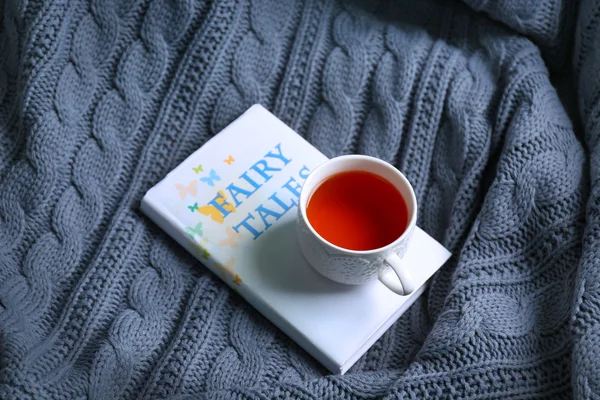 A book and a cup of tea on knitted blanket. Peace and comfort concept
