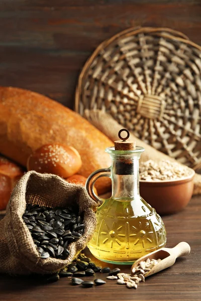 Composition of sunflower seeds, bread and oil on wooden table background, closeup