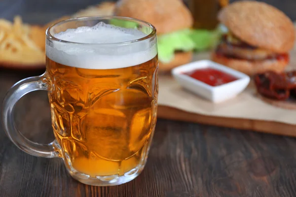 Glass mug of light beer with snacks on dark wooden table, close up