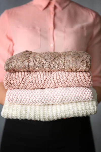 Stack of knitted clothes in female hands closeup