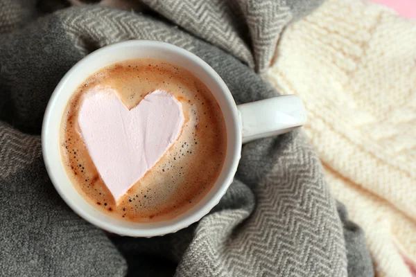 Cup of hot cappuccino with heart marshmallow and warm clothes, close up