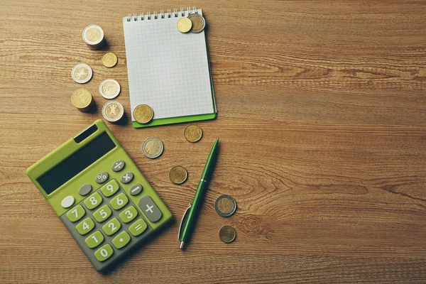 Money concept. Green calculator with coins and notebook on wooden table