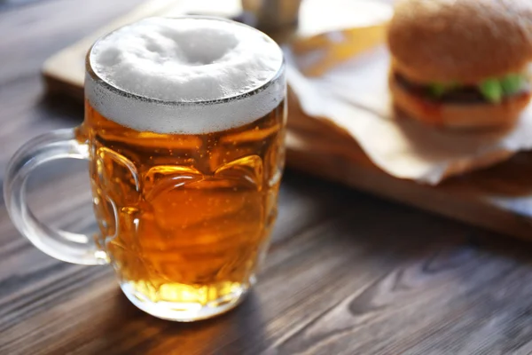 Glass mug of light beer with hamburger on dark wooden table, close up