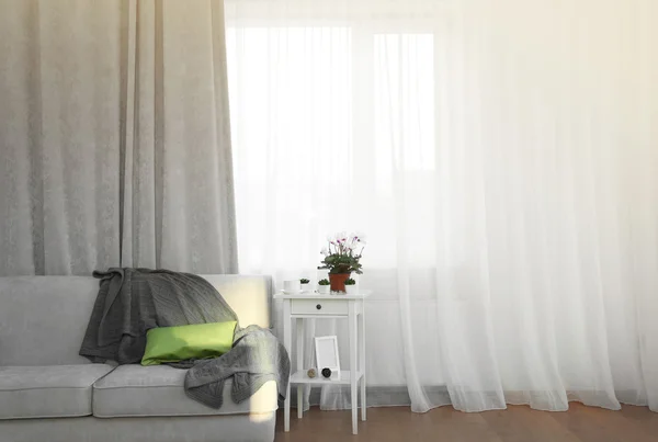 Grey sofa and small table with flowers on curtain background