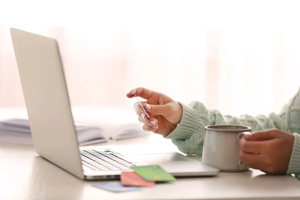 E-commerce concept. Woman with credit card, laptop and cup of coffee, close up