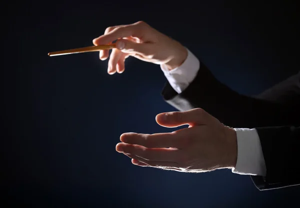 Music conductor directing with baton on black lightened background, close up