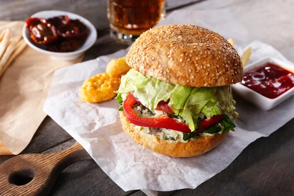 Big tasty hamburger with snacks and glass mug of light beer on wooden table