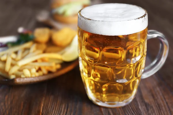 Glass mug of light beer with French fries on dark wooden table, close up