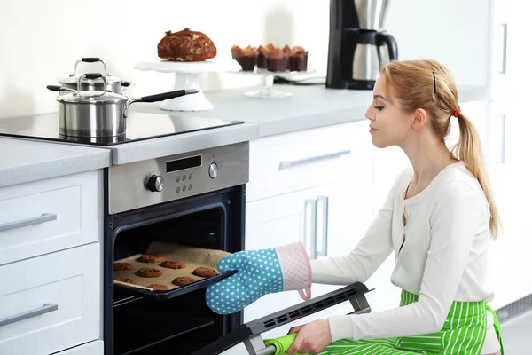 Young woman removing cookie tray from the oven in a kitchen