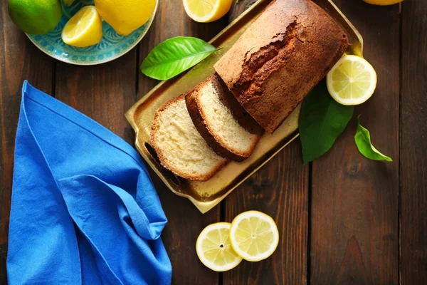 Delicious sweet cake bread in metal tray with lemons on wooden table, top view