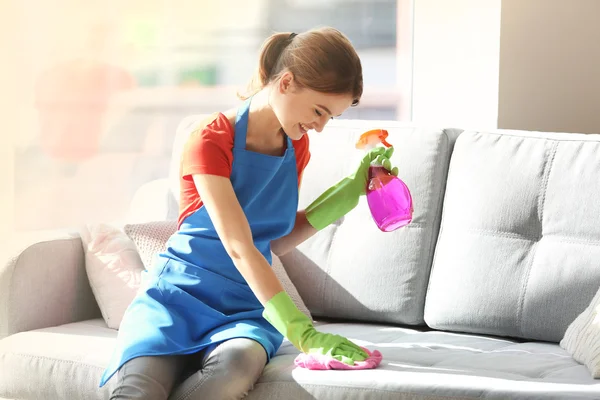 Young woman cleans sofa in room