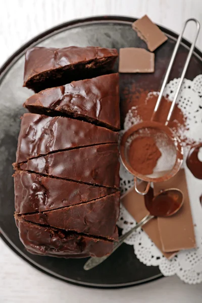 Chocolate sliced cake with icing and cocoa powder on baking dish over white table