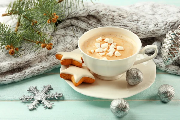 Cup of hot cacao with marshmallow, cookies and warm scarf on blue table