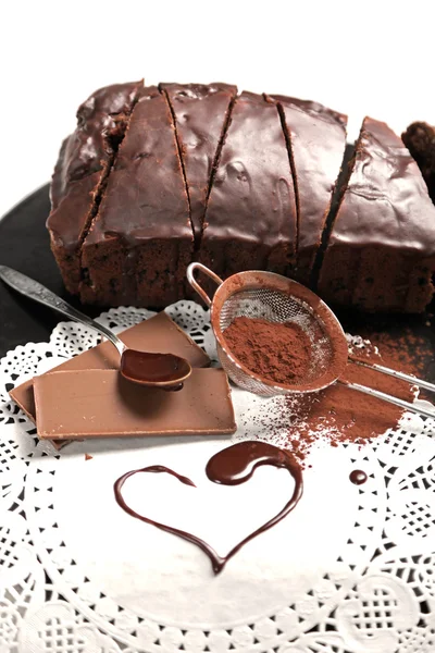 Chocolate sliced cake with icing and cocoa powder on baking dish over white table