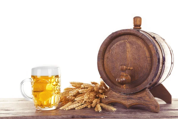 Beer barrel and glass of beer with wheat on wooden table against white background