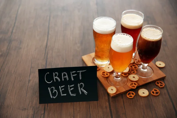 Glasses with different sorts of craft beer and snacks on wooden tray