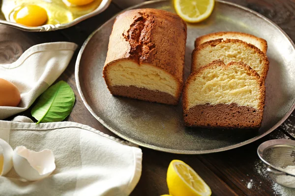 Delicious sweet cake bread in metal tray with lemons on wooden table closeup