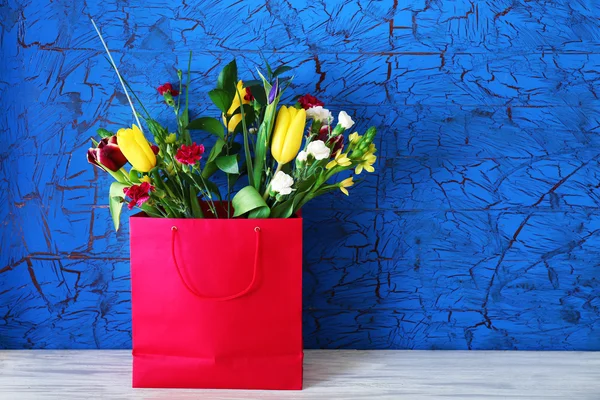Bouquet of fresh flowers in a bag on blue background