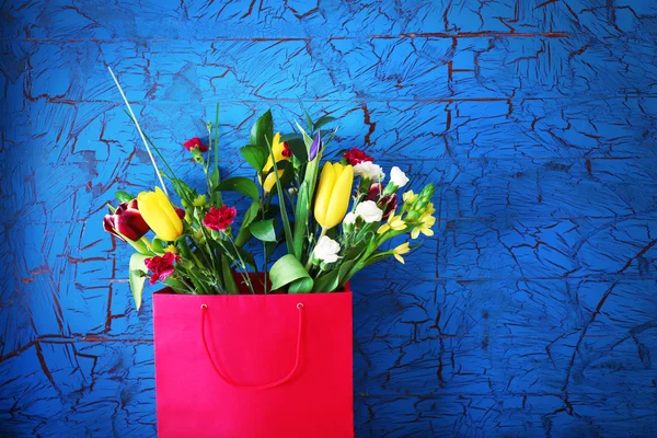 Bouquet of fresh flowers in a bag over blue wall