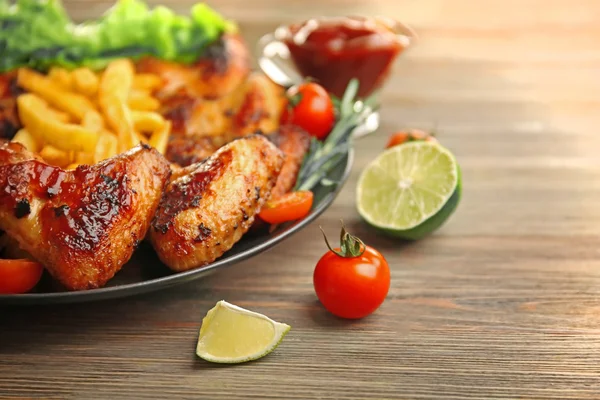 Grilled chicken wings with French fries, garden-staff and tomatoes on plate