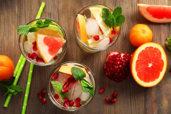 Refreshing cocktails with ice, mint, pomegranate seeds and slices of fruits on wooden background