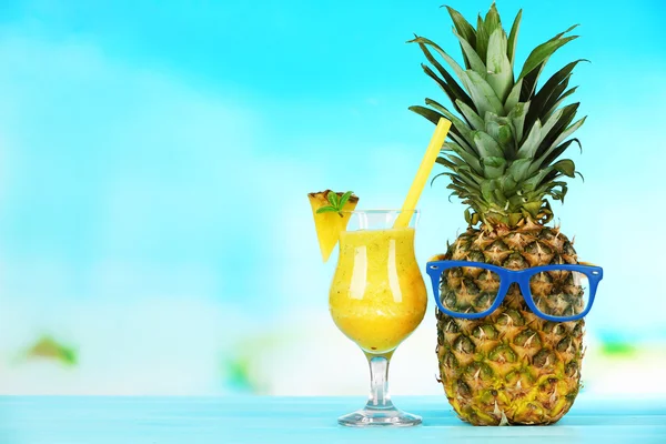 Ripe pineapple with glasses and smoothie in glass on blue blurred background