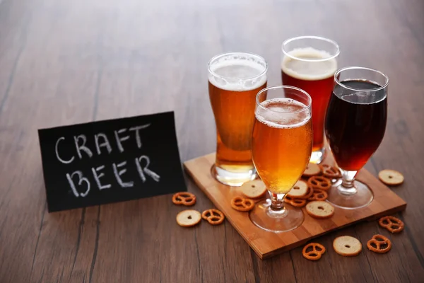 Glasses with different sorts of craft beer and snacks on wooden tray