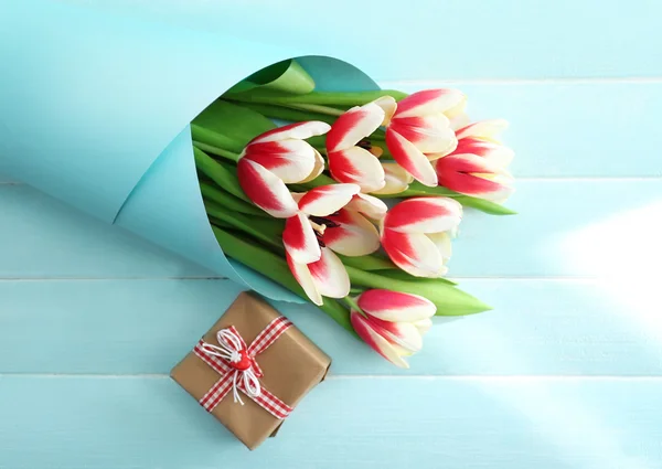 Bouquet of variegated tulips wrapped in paper with gift box on blue wooden background
