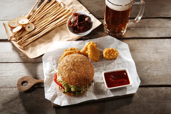 Big tasty hamburger with snacks and glass mug of light beer on wooden table