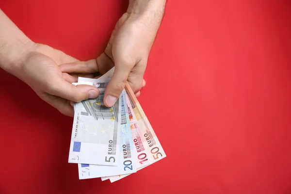 Male hands counting euro banknotes on red background