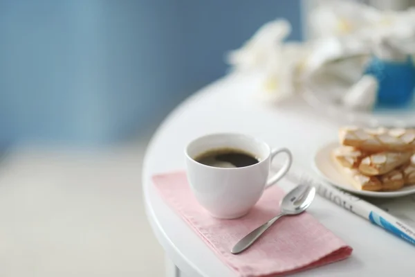 Cup of coffee with cookies on white table in light interior