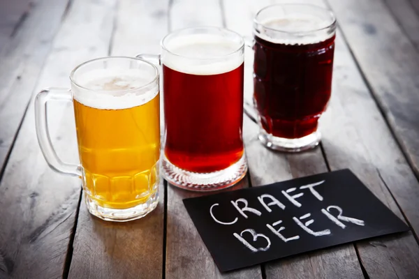 Glass mugs with different sorts of craft beer on wooden table. Retro stylization