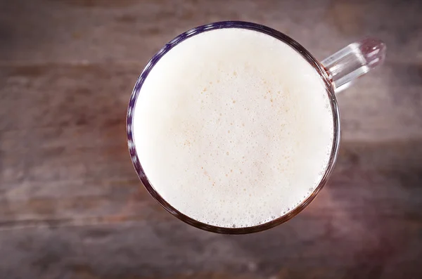 Top view of glass mug of light beer with foam on wooden table. Retro stylization