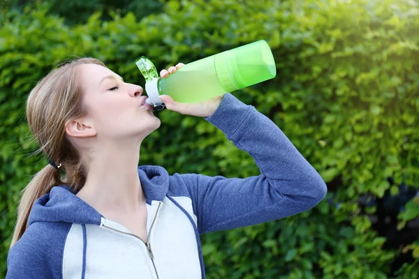 Sporty woman drinking water after jogging at park on a sunny day