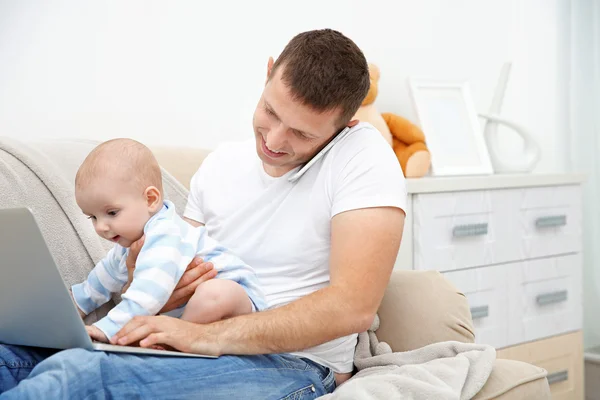 Father working on laptop and holding baby
