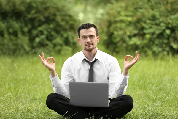 Businessman with laptop relaxing in meditation pose