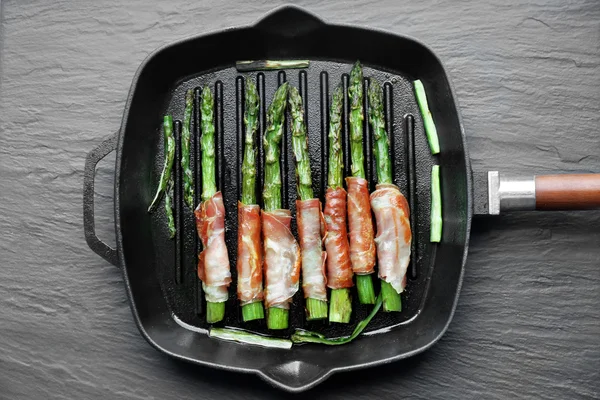 Asparagus with bacon on frying pan